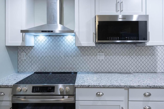 kitchen with light stone countertops, appliances with stainless steel finishes, white cabinets, and wall chimney exhaust hood