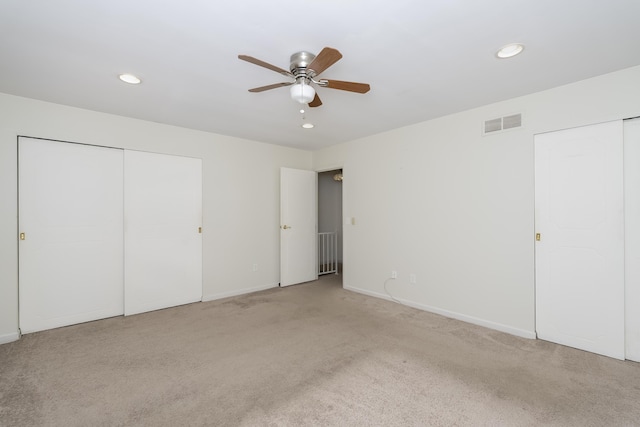 unfurnished bedroom with multiple closets, ceiling fan, and light colored carpet