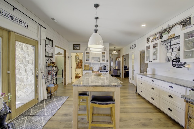 kitchen with a breakfast bar, white cabinetry, light stone counters, a center island, and pendant lighting