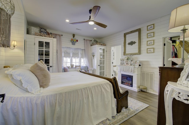 bedroom featuring hardwood / wood-style floors, ceiling fan, and wood walls