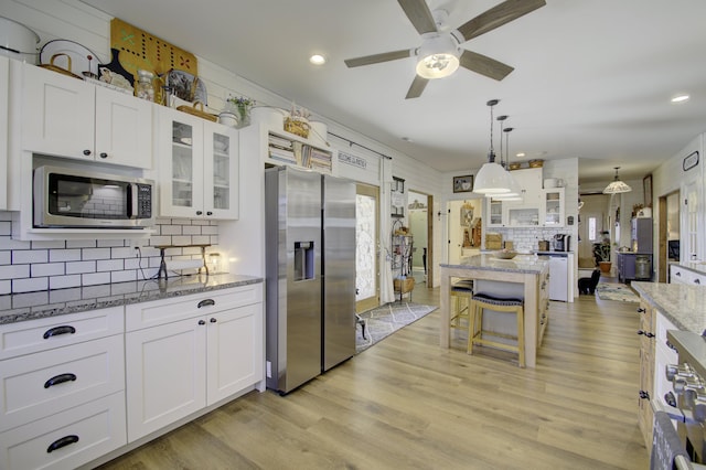 kitchen featuring hanging light fixtures, light stone countertops, white cabinets, and appliances with stainless steel finishes