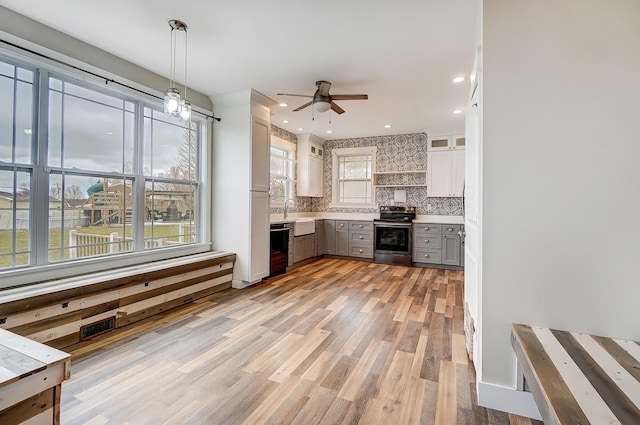 kitchen with stainless steel electric stove, light countertops, gray cabinetry, light wood-type flooring, and dishwashing machine