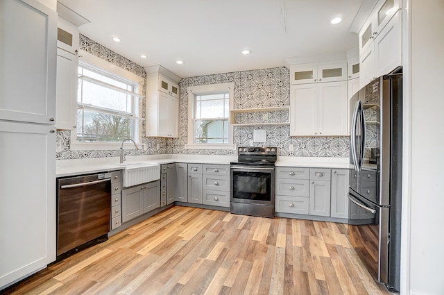 kitchen with gray cabinetry, a sink, light wood-style floors, light countertops, and appliances with stainless steel finishes