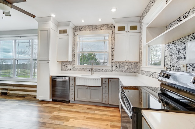 kitchen with light wood-style flooring, stainless steel appliances, a sink, light countertops, and tasteful backsplash