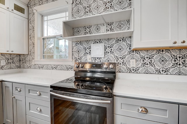 kitchen featuring glass insert cabinets, gray cabinetry, stainless steel range with electric stovetop, open shelves, and backsplash