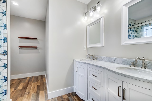 bathroom with double vanity, baseboards, a sink, and wood finished floors