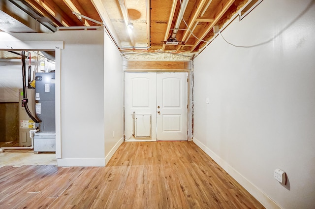 unfinished below grade area with water heater, light wood-type flooring, and baseboards