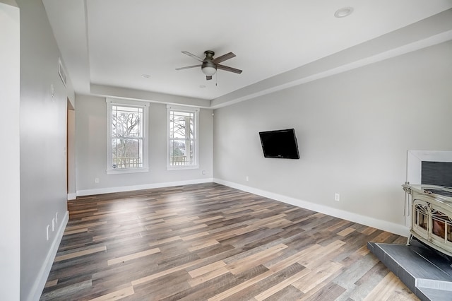 unfurnished living room with ceiling fan, wood finished floors, visible vents, baseboards, and a wood stove