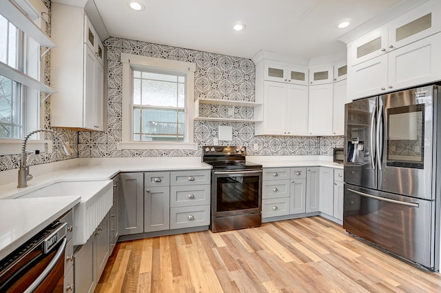 kitchen with light wood finished floors, open shelves, gray cabinets, appliances with stainless steel finishes, and a sink