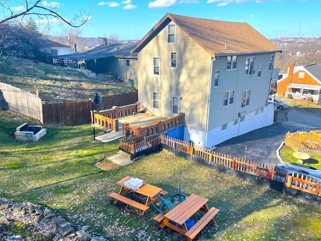 exterior space featuring a fenced backyard, driveway, roof with shingles, a lawn, and a wooden deck