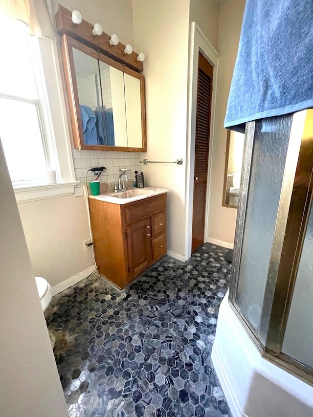 bathroom with baseboards, vanity, decorative backsplash, and combined bath / shower with glass door