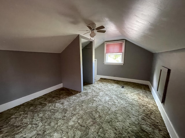 additional living space with vaulted ceiling, dark colored carpet, and ceiling fan