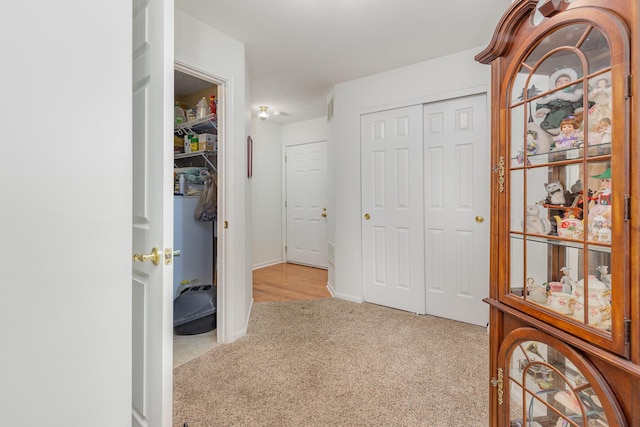 corridor with baseboards, visible vents, and light colored carpet