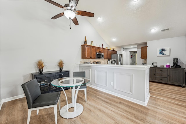 kitchen featuring kitchen peninsula, appliances with stainless steel finishes, backsplash, and light hardwood / wood-style floors