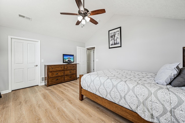 bedroom featuring light wood-type flooring, vaulted ceiling, ceiling fan, and a textured ceiling