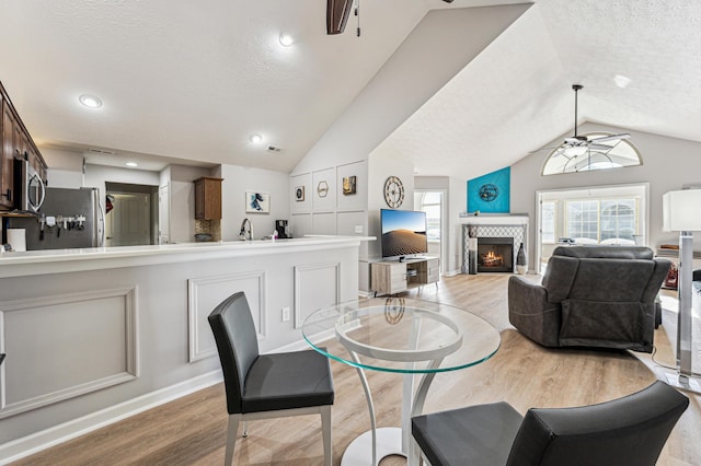 dining space featuring a fireplace, ceiling fan, light wood-type flooring, and vaulted ceiling