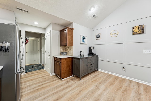 kitchen with light hardwood / wood-style flooring, backsplash, stainless steel fridge, and lofted ceiling