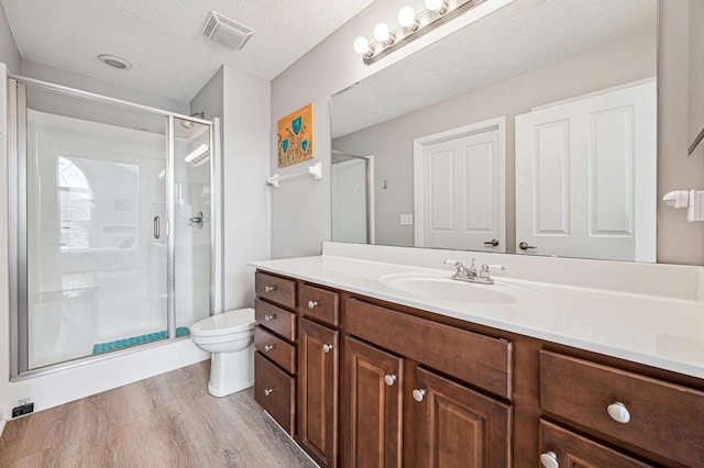 bathroom featuring wood-type flooring, toilet, a textured ceiling, an enclosed shower, and vanity