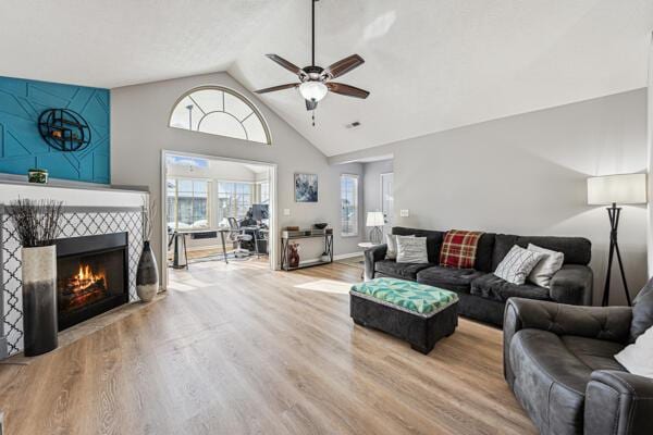 living room with ceiling fan, high vaulted ceiling, wood-type flooring, and a tiled fireplace