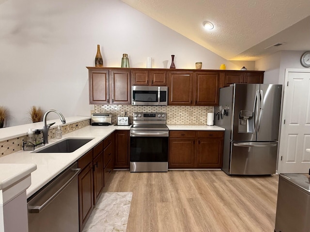 kitchen featuring vaulted ceiling, stainless steel appliances, light hardwood / wood-style flooring, and sink