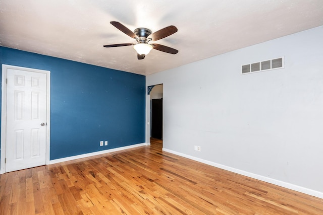 spare room with a ceiling fan, wood finished floors, visible vents, and baseboards