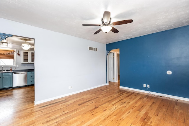 empty room with light wood finished floors, baseboards, visible vents, a ceiling fan, and a sink