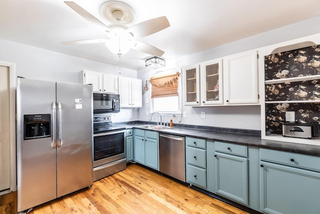 kitchen with stainless steel appliances, dark countertops, a sink, and white cabinets