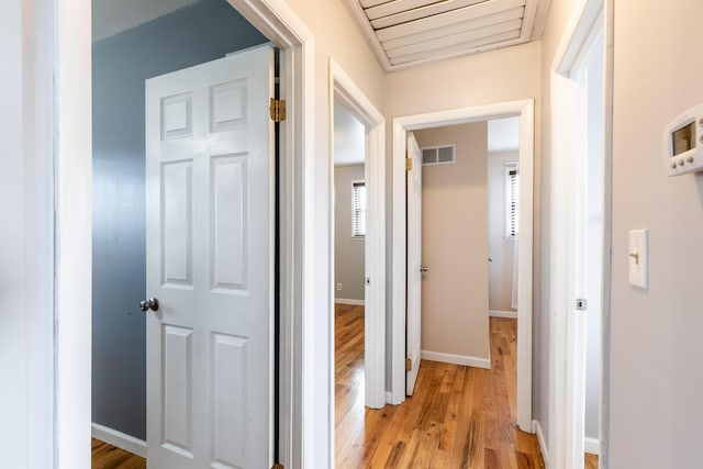 hall with visible vents, light wood-style flooring, and baseboards