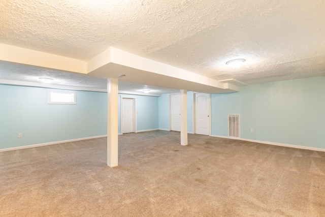 basement with a textured ceiling, carpet, visible vents, and baseboards