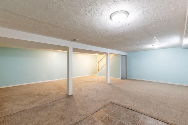 finished basement featuring stairs, a textured ceiling, carpet, and baseboards