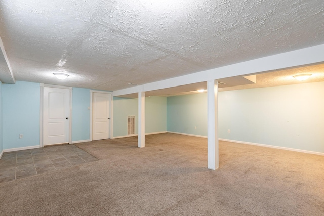 finished basement featuring carpet floors, visible vents, baseboards, and a textured ceiling