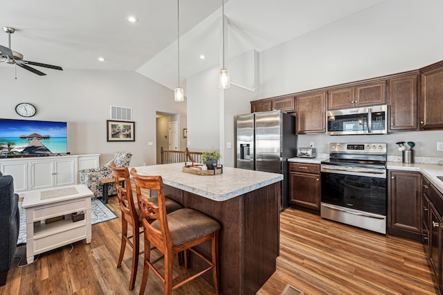 kitchen with dark brown cabinets, a kitchen breakfast bar, stainless steel appliances, pendant lighting, and a center island