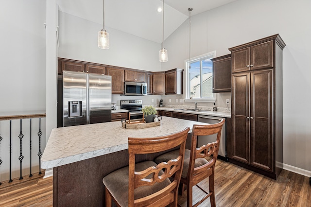 kitchen with dark hardwood / wood-style flooring, a kitchen island, sink, appliances with stainless steel finishes, and pendant lighting