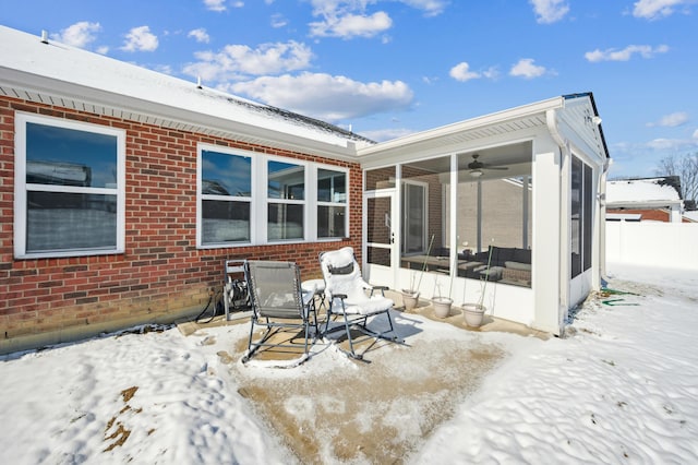 snow covered house featuring ceiling fan and a sunroom