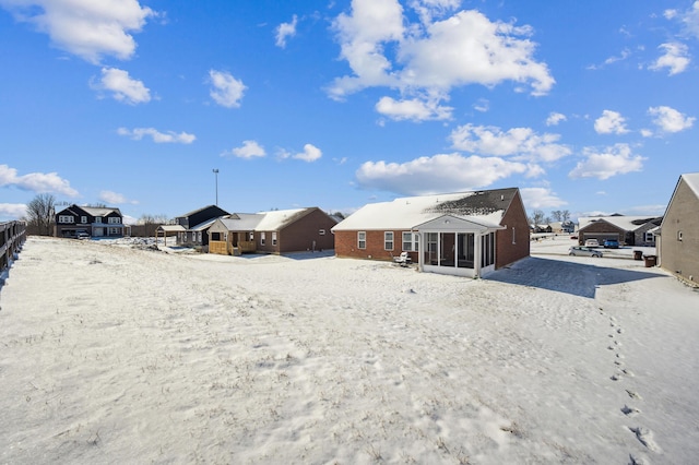 snow covered back of property featuring a sunroom