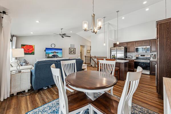 dining space with dark wood-type flooring, high vaulted ceiling, and ceiling fan with notable chandelier