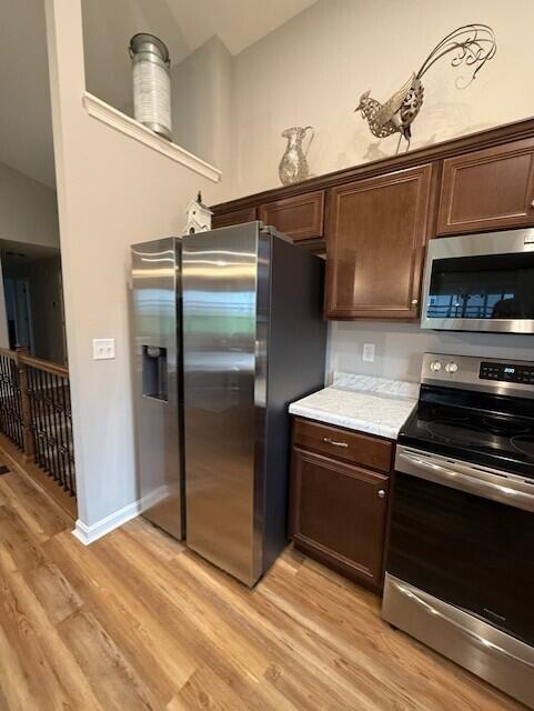 kitchen featuring dark brown cabinets, light hardwood / wood-style flooring, stainless steel appliances, and vaulted ceiling