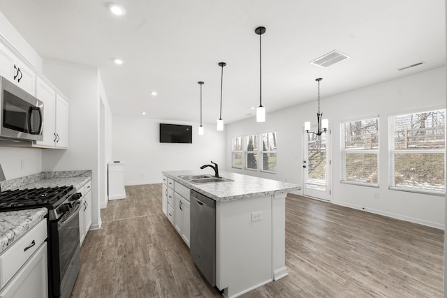 kitchen featuring hanging light fixtures, stainless steel appliances, white cabinets, sink, and a kitchen island with sink