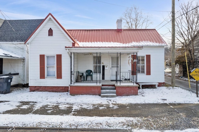 bungalow-style home featuring covered porch, a chimney, and metal roof