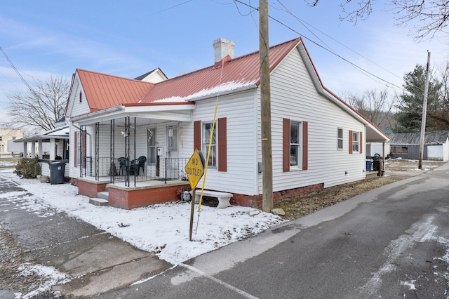 view of snowy exterior with metal roof, a porch, and a chimney