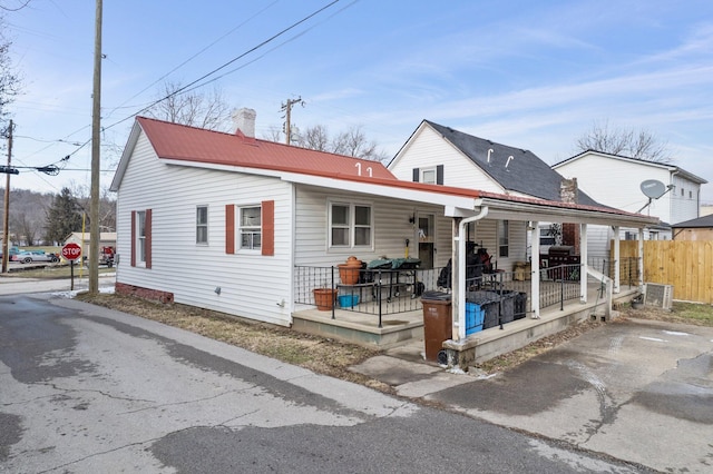 view of front of property featuring a porch, metal roof, a chimney, and fence