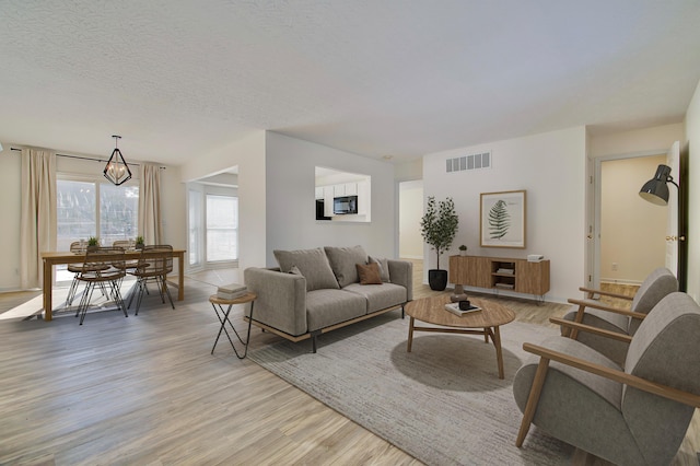 living room with visible vents, a notable chandelier, light wood-style flooring, and a textured ceiling