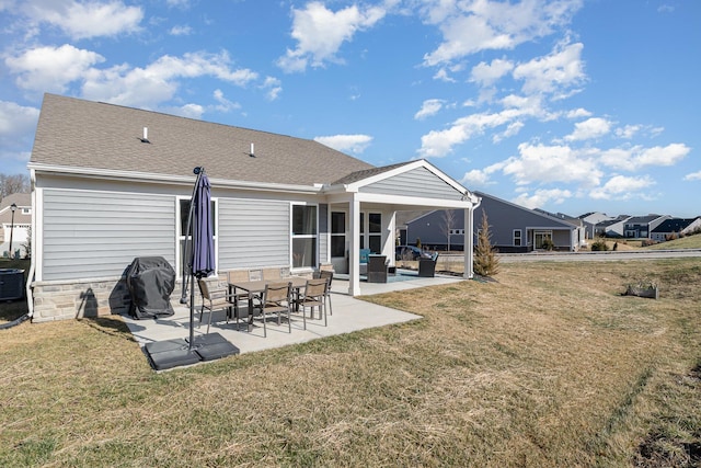 back of house with a shingled roof, a lawn, and a patio
