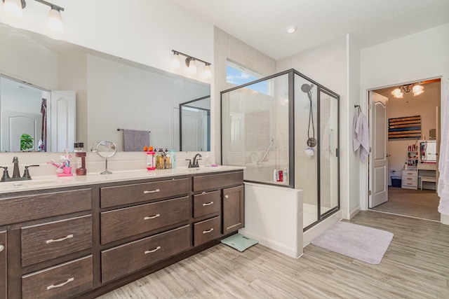 ensuite bathroom featuring double vanity, a sink, a shower stall, and wood finished floors