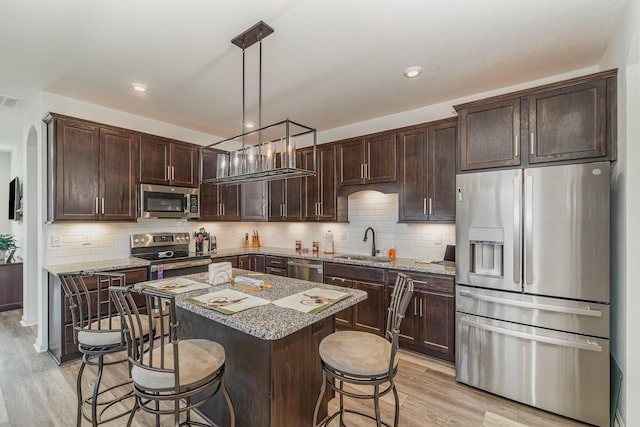 kitchen with a sink, a kitchen breakfast bar, appliances with stainless steel finishes, a center island, and pendant lighting