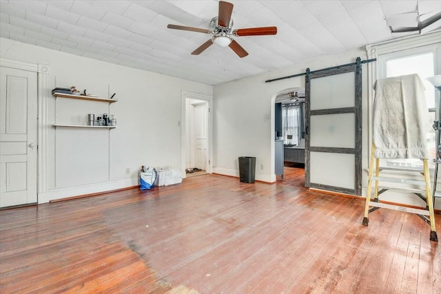 interior space with a barn door, arched walkways, ceiling fan, and wood finished floors