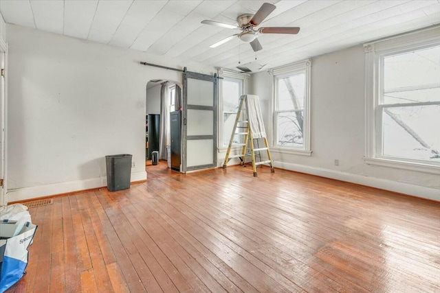 empty room with a barn door, wood finished floors, a ceiling fan, and baseboards