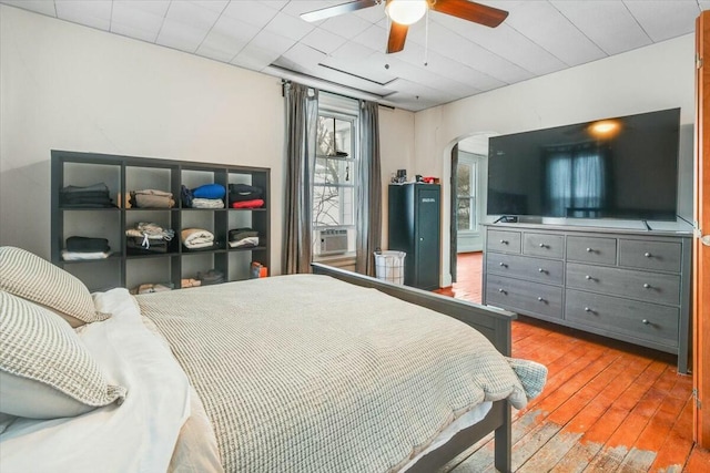 bedroom with a ceiling fan, cooling unit, arched walkways, and wood finished floors