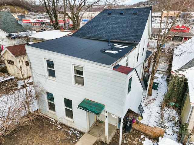 snow covered property with roof with shingles