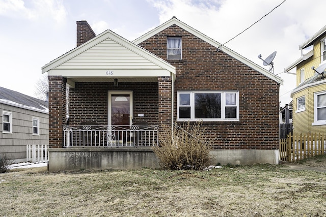 view of front of property with a porch, brick siding, fence, a front lawn, and a chimney